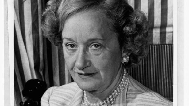 Hattie Carnegie trägt eine Perlenkette und einen gestreiften Blazer.