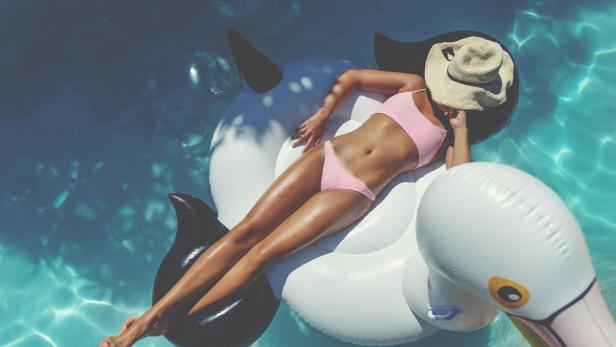 Eine Frau mit Hut entspannt auf einer aufblasbaren Schwimmhilfe im Pool.