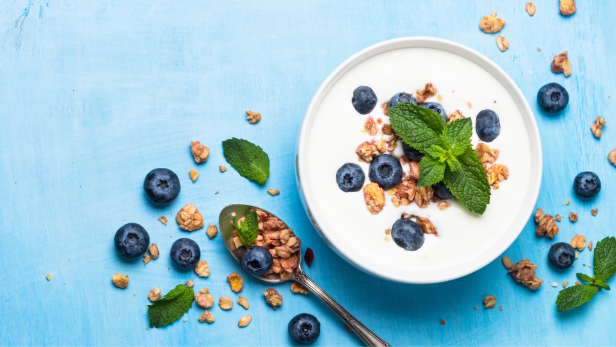 Joghurt mit Blaubeeren, Müsli und Minze auf einem blauen Tisch.