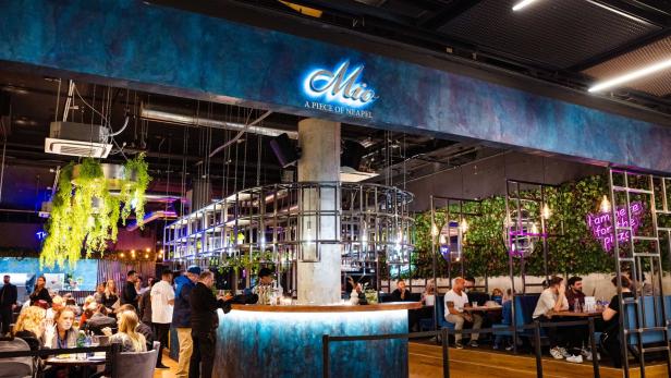 Innenansicht des Restaurants „Mio A Piece of Neapel“ mit Gästen an Tischen und an der Bar.