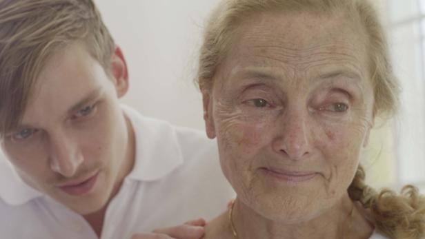 Ein junger Pfleger legt einer älteren Dame tröstend die Hand auf die Schulter.