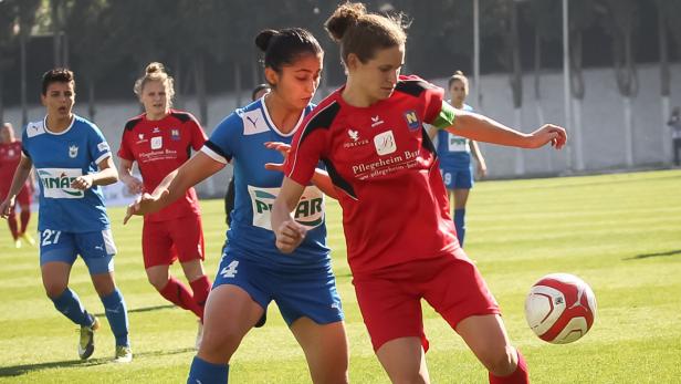 Zwei Fußballspielerinnen kämpfen um den Ball auf dem Spielfeld.