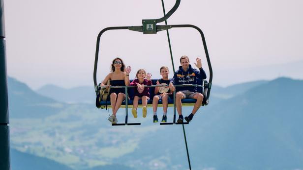 Eine Familie fährt gemeinsam in einem Sessellift über eine Berglandschaft.
