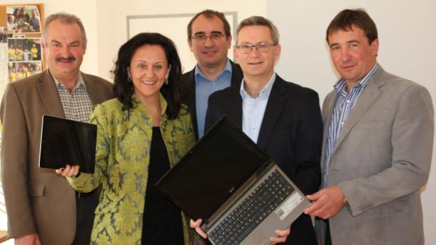 Eine Gruppe von fünf Personen posiert mit einem Tablet und einem Laptop für ein Foto.