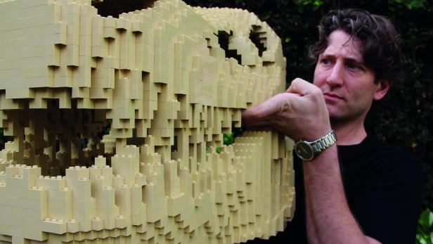 Ein Mann berührt einen Dinosaurierschädel, der aus hellbeigen Legosteinen gebaut wurde.