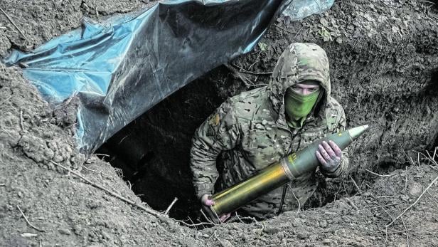 Vermummter Ukrainischer Soldat im Graben mit einem Artillerie-Geschoss