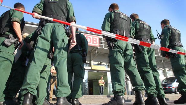 Polizisten stehen vor einem DB-Gebäude hinter einem rot-weißen Absperrband.