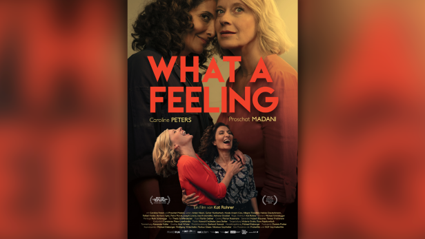 Filmplakat von "What a Feeling", man sieht die beiden Hauptdarstellerinnen einander zugeneigt und lachend