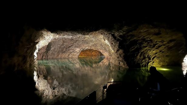 Eine dunkle Grotte mit grünlichem Wasser wird von Felswänden und schwachem Licht umgeben.