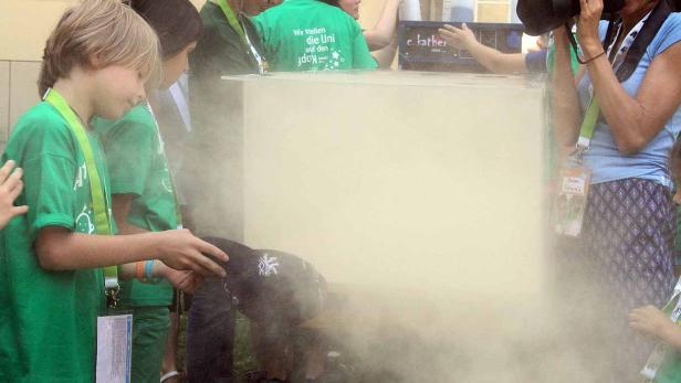 Kinder experimentieren mit Trockeneis, während eine Frau Fotos macht.