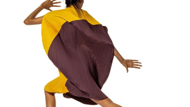 Eine Frau in einem plissierten, farblich geteilten Kleid posiert auf einem weißen Hintergrund.