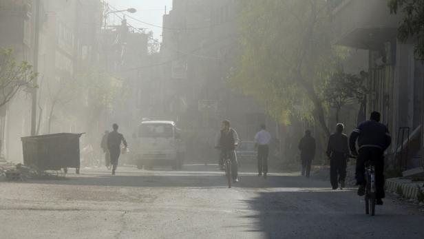 Eine staubige Straße mit Menschen, einem Fahrradfahrer und einem Lieferwagen.