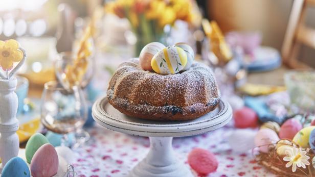 Ein gedeckter Ostertisch mit einem Gugelhupf und bemalten Eiern.