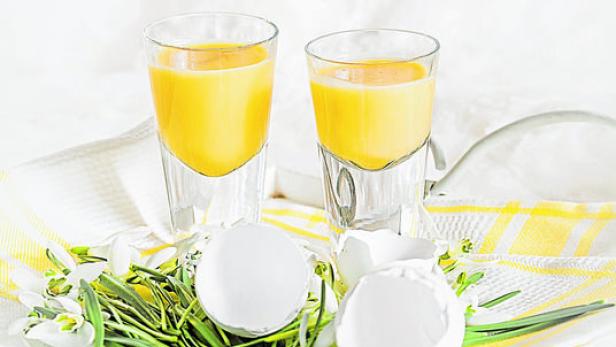 Zwei Gläser Eierlikör stehen mit Eierschalen und Schneeglöckchen auf einem Tablett.