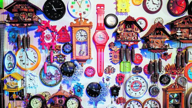 Symbolbild Zeitumstellung: Eine Wand voller Wanduhren, Kuckucksuhren, FC-Bayern-Uhr, übergroße pinke Armbanduhr