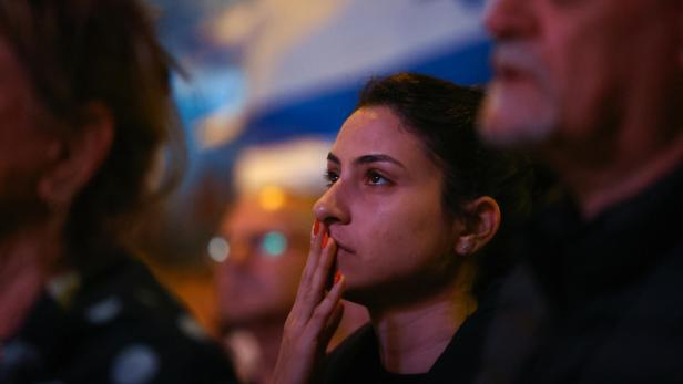 Frau hält sich bei einer Demo in Israel Hand vor den Mund, im Hintergrund Israel-Flagge