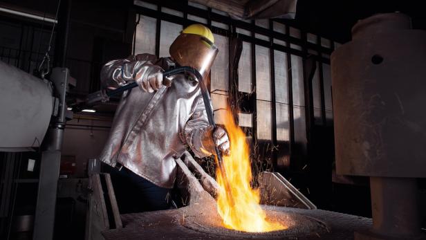 Ein Arbeiter in Schutzkleidung gießt flüssiges Metall in einer Gießerei.