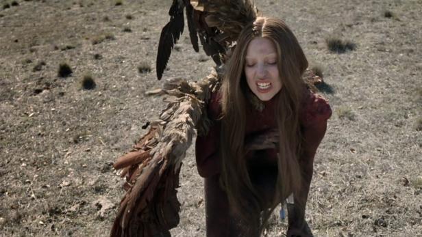 Eine Frau mit Flügeln schreit in einem kargen Feld.