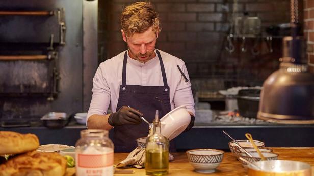 Ein Koch bereitet in einer Küche ein Gericht zu.