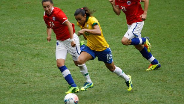 Eine brasilianische Fußballspielerin dribbelt den Ball, verfolgt von zwei chilenischen Spielerinnen.