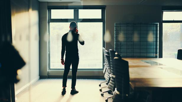 Rearview shot of a young businessman talking on a cellphone in an empty boardroom