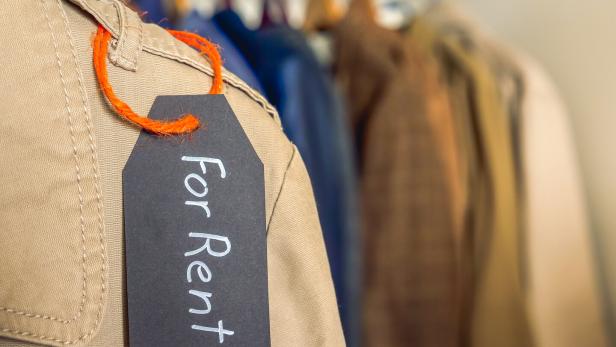 Ein Kleiderbügel mit mehreren Kleidungsstücken, an einem davon hängt ein Schild mit der Aufschrift „For Rent“.