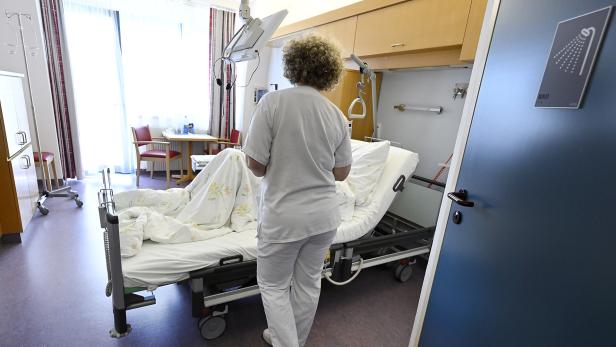 Eine Krankenschwester steht am Bett eines Patienten in einem hellen Krankenzimmer.