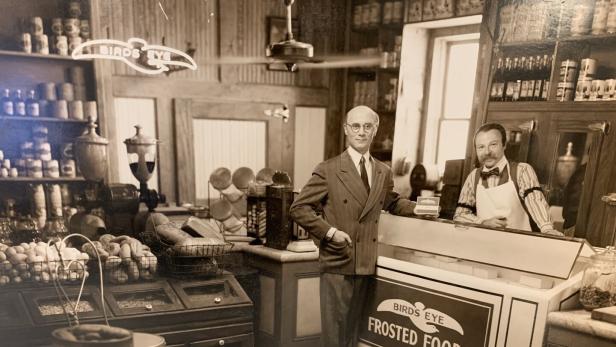 Ein Mann im Anzug und ein Verkäufer stehen in einem „Birds Eye Frosted Foods“-Laden.