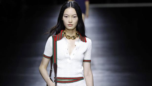 Eine Frau in einem weißen, sportlichen Outfit mit grünen und roten Akzenten auf einem Laufsteg.