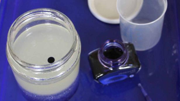 Ein Glas mit einer Flüssigkeit und Tinte auf einem blauen Untergrund.