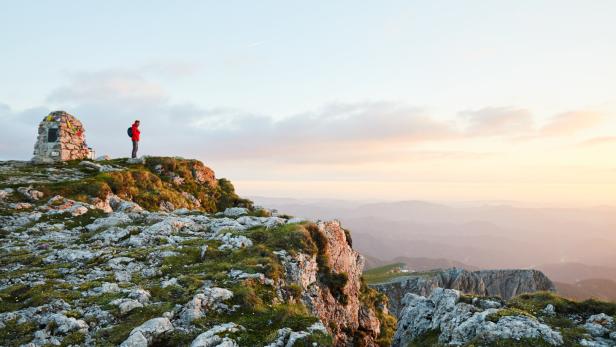 Ein Wanderer steht auf dem Gipfel des Schneebergs neben einem Steinhaufen.