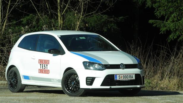 Ein weißer VW Polo mit blauen Streifen steht vor einem Wald.