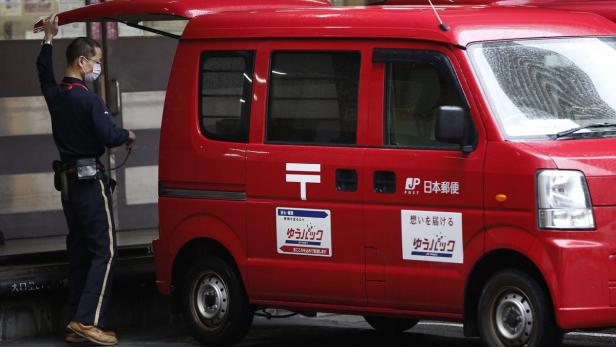 Ein Postbote mit Maske steht neben einem roten Lieferwagen der japanischen Post.