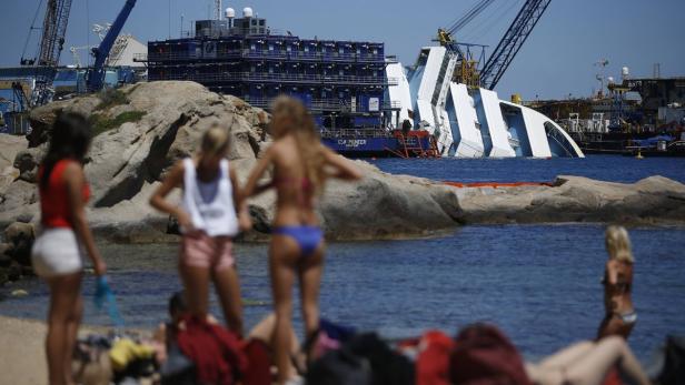 People stand on the beach as the capsized cruise l