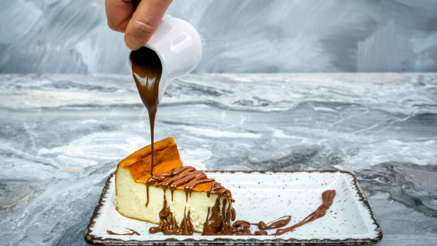 Ein Stück Käsekuchen wird mit Schokoladensoße übergossen.