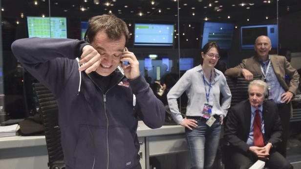 Ein Mann telefoniert aufgeregt, während drei weitere Personen im Hintergrund stehen.