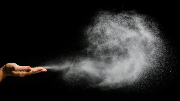 Eine Hand wirft eine Wolke aus weißem Pulver in die Luft.
