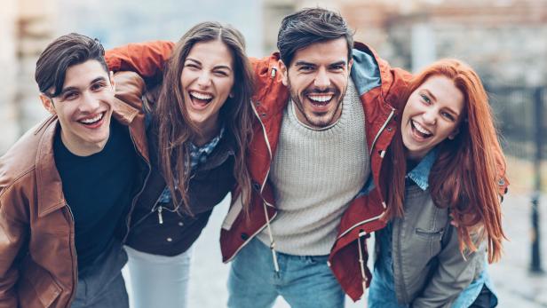 Vier lachende Freunde umarmen sich im Freien.