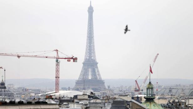 Die Skyline von Paris mit dem Eiffelturm und mehreren Baukränen im Dunst.