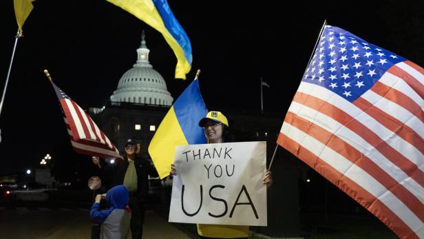 Menschen mit Ukraine- und USA-Flaggen stehen vor dem Kapitol in Washington und halten ein Schild mit  der Aufschrift "Thank You USA"