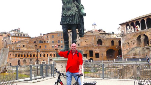 Mann steht mit Fahrrad vor der Caesar-Statue in Rom und macht seine Pose nach