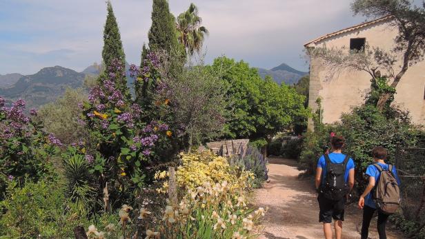 Wanderndes Paar auf Mallorca, im Hintergrund Berge, eine üppige Landschaft und ein Steinhaus