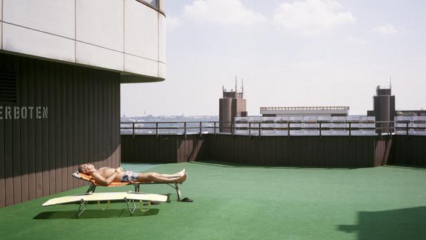 Ein Mann liegt auf einer Liege auf einem Dach mit grünem Bodenbelag.