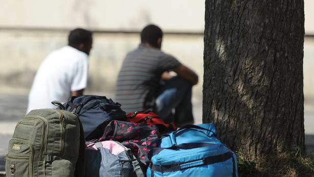 Zwei Männer sitzen hinter einem Berg von Gepäck, man sieht sie nur von hinten.