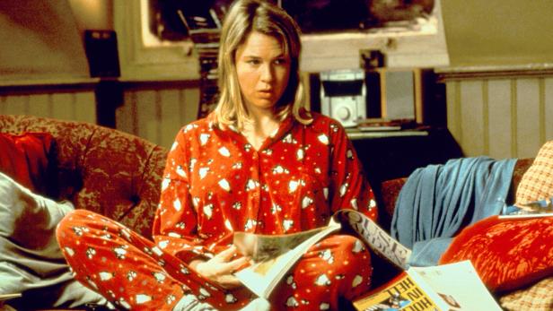 Eine Frau (die Figur Bridget Jones, gespielt von Renee Zellweger) sitzt im roten Pyjama auf ihrer Couch und blättert in einer Zeitschrift