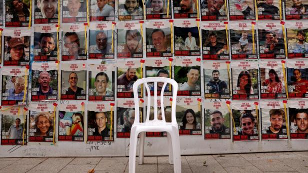 Weißer Plastikstuhl steht vor Wand mit Plakaten von Hamas-Geiseln