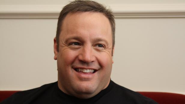 Ein lächelnder Kevin James vor einer hellen Wand.