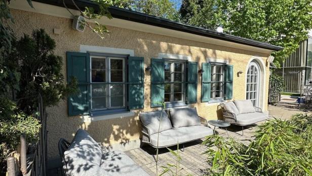 Ein gelbes Gebäude mit grünen Fensterläden und einer Terrasse mit Gartenmöbeln.