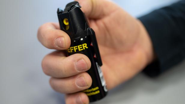 Eine Hand hält eine schwarze Pfefferspraydose mit gelber Aufschrift und bereitet sich auf die Benutzung vor.