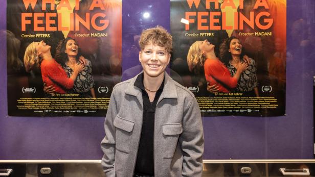 Eine Person steht vor Postern für den Film „What a Feeling“ mit Caroline Peters und Proschat Madani.